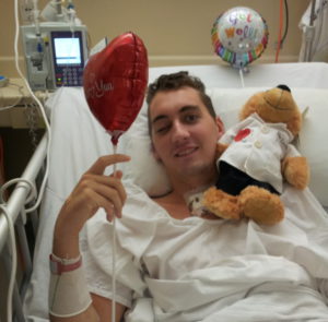 Trent laying in hospital bed with balloon and teddy bear