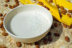 Small white bowl of milk with almonds scattered beside