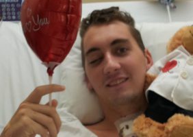 Trent laying in hospital bed with balloon and teddy bear