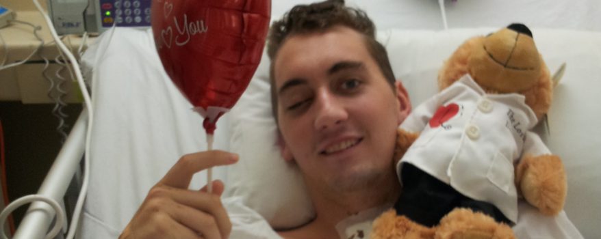 Trent laying in hospital bed with balloon and teddy bear