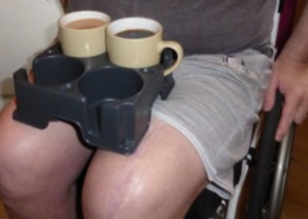 Muggi with cups of tea on the lap of a wheelchair user