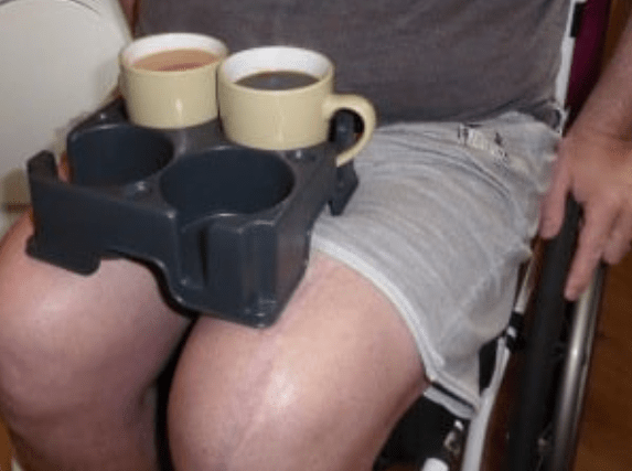 Muggi with cups of tea on the lap of a wheelchair user