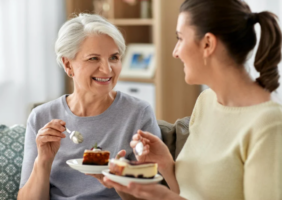 Adult daughter eating cake with her elderly mother