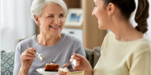 Adult daughter eating cake with her elderly mother