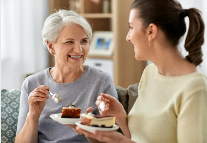 Adult daughter eating cake with her elderly mother